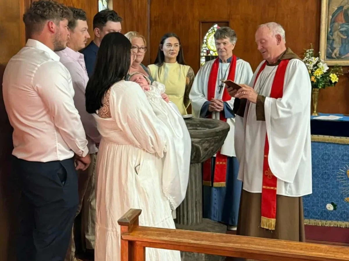 Family gathered around the stone font as an infant is presented for baptism at The Abbey Church